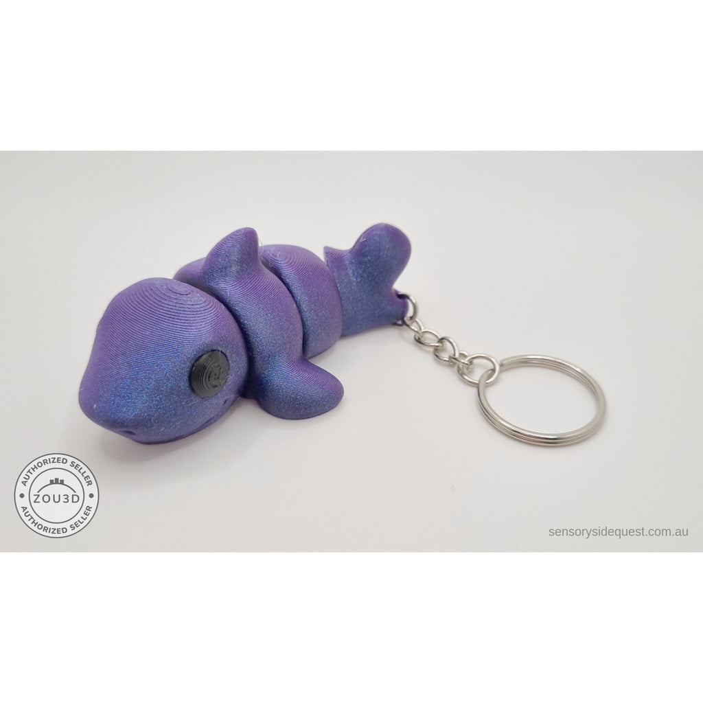 027-TNYSHK Tiny Shark keychain in crushed electric purple — 3/4 front view showing iridescent purple-to-blue shimmer, chibi face, dorsal fin, and keychain — 3D printed fidget toy by Sensory Sidequest