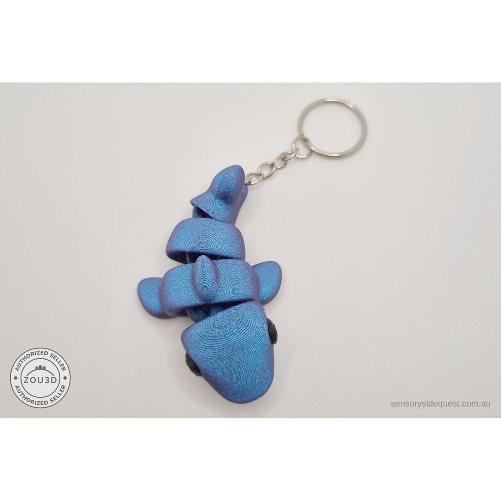 027-TNYSHK Tiny Shark keychain in gentian blue — angled flat view showing metallic iridescent deep blue shimmer with keychain ring — 3D printed articulated fidget toy by Sensory Sidequest