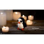 Penguin articulated fidget toy designer lifestyle render, 3/4 view with candlelight, white and black with orange beak and feet — 3D printed articulated fidget toy by Sensory Sidequest