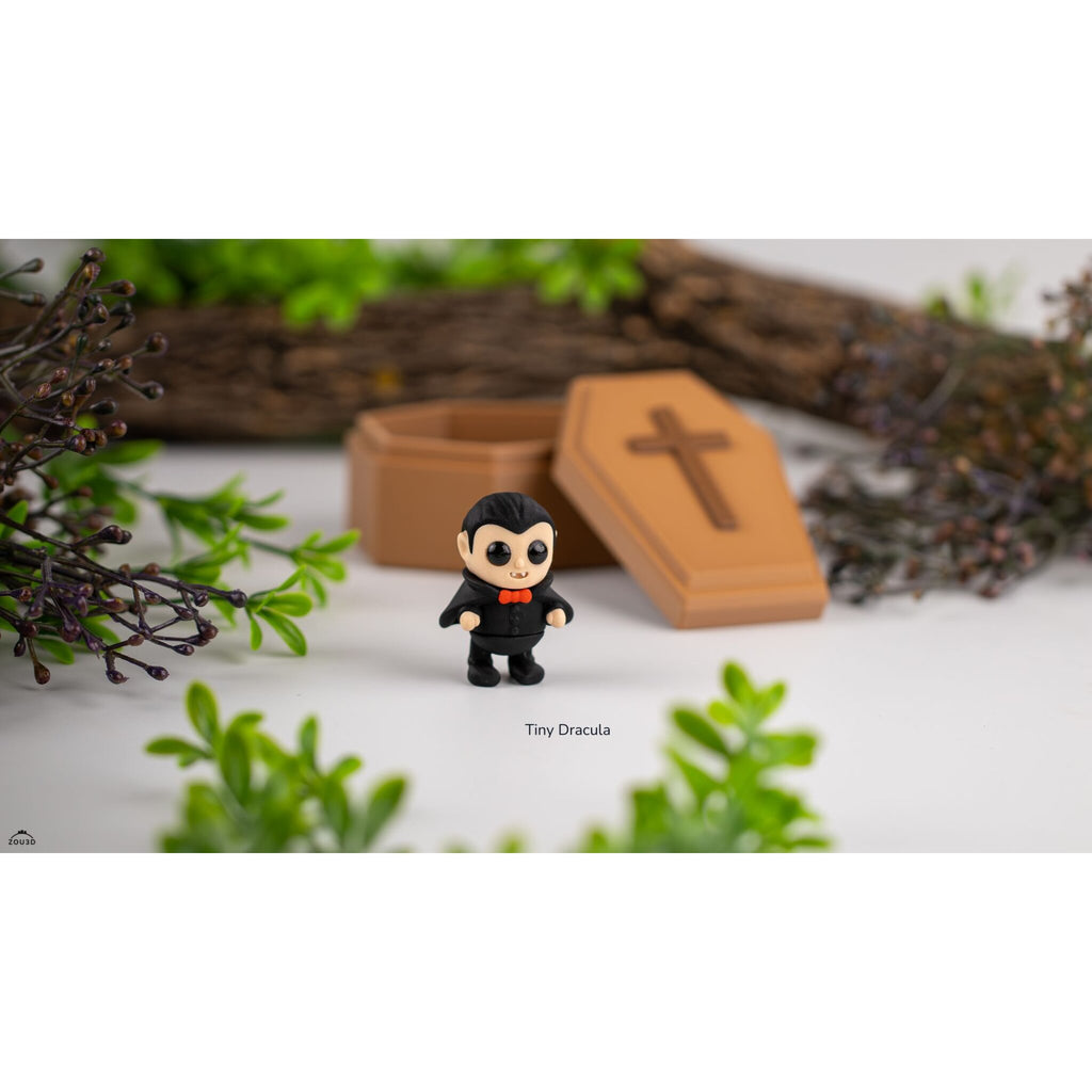 Tiny Dracula 3D printed articulated figure standing in front of open wooden coffin prop with Halloween foliage