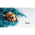 Baby Spider 3D printed fidget toy sitting in a nest of turquoise yarn — overhead angle showing rounded body segments and expressive eyes