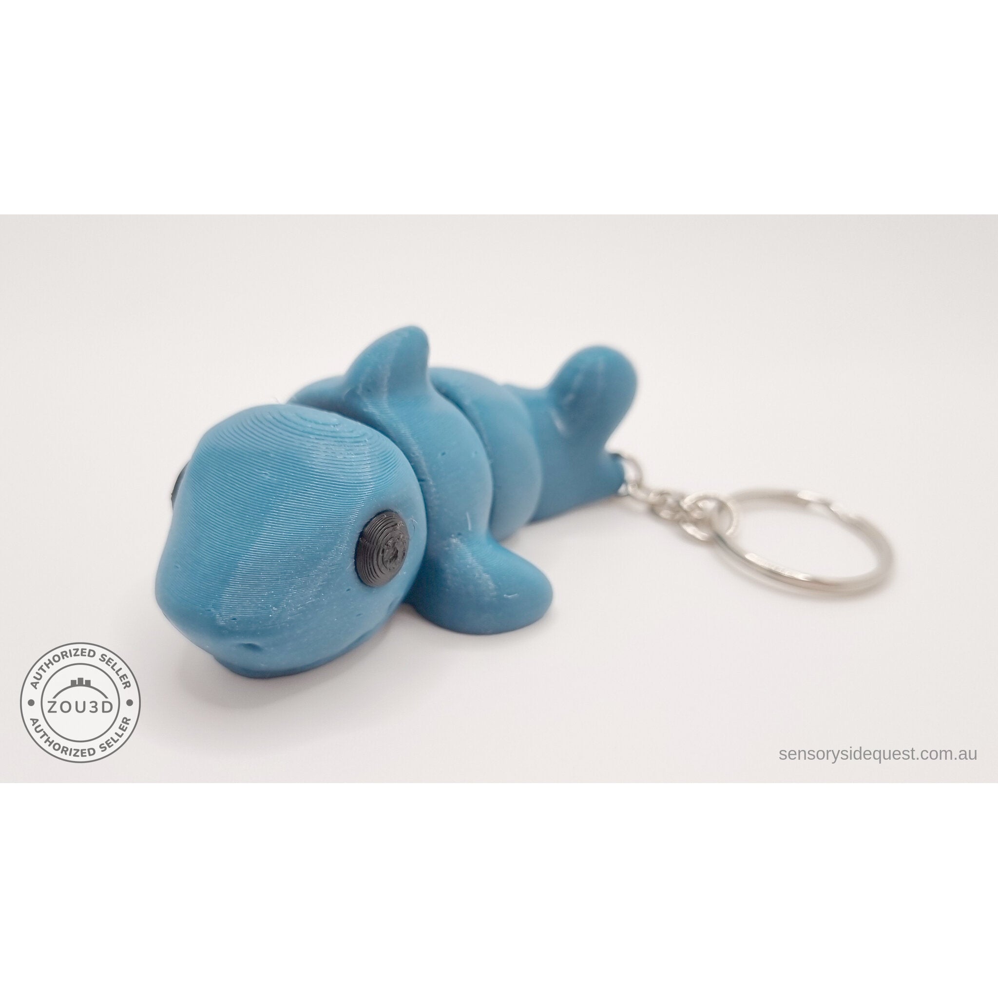027-TNYSHK Tiny Shark keychain in gentian blue — 3/4 front view showing chibi face, dorsal fin, articulated body, and keychain hardware — 3D printed fidget toy by Sensory Sidequest