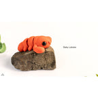 Baby Lobster articulated fidget toy — official Zou3D render, side view on rock prop with plant props, orange colourway