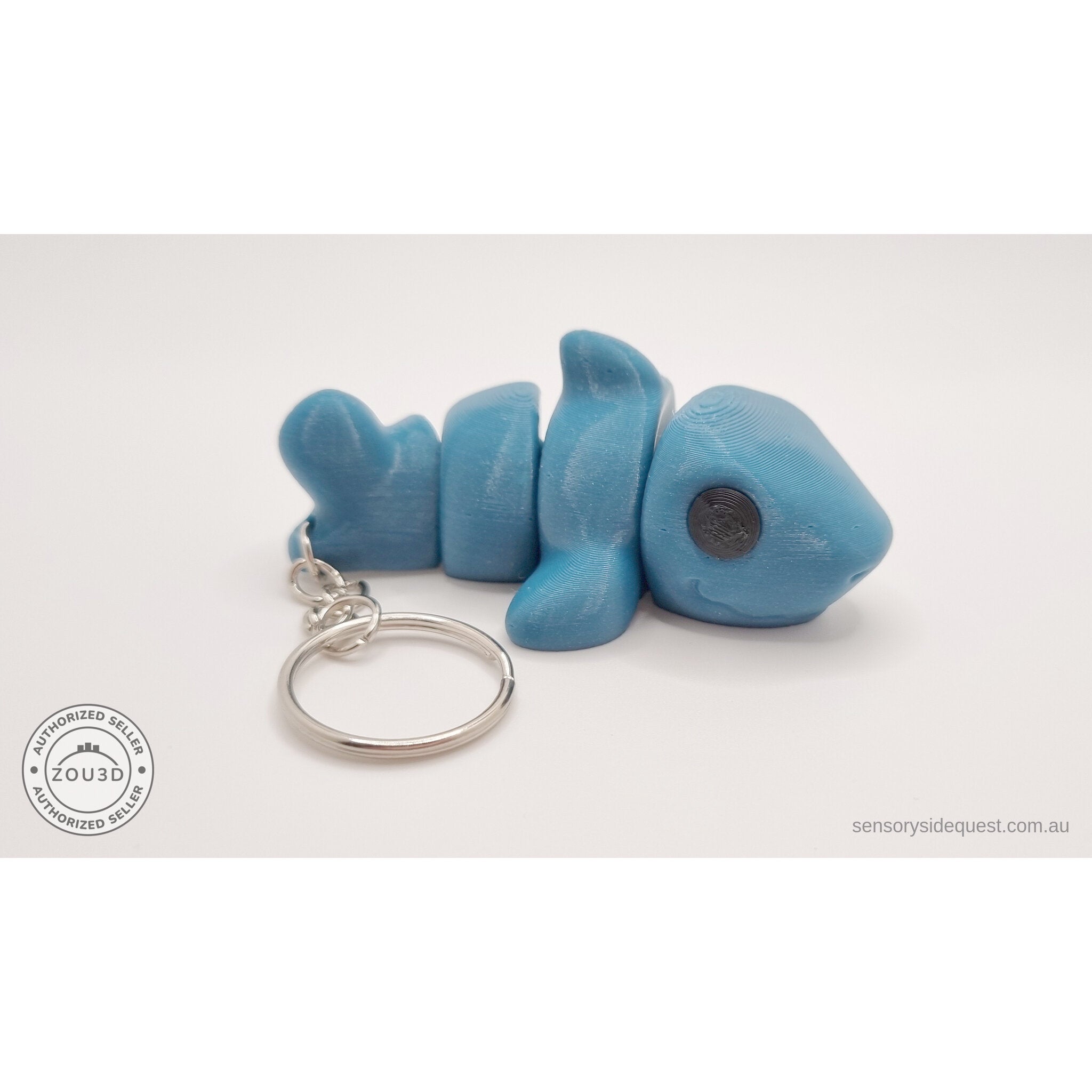 027-TNYSHK Tiny Shark keychain in gentian blue — side view with body coiled tightly, showing full articulation range — 3D printed fidget toy by Sensory Sidequest